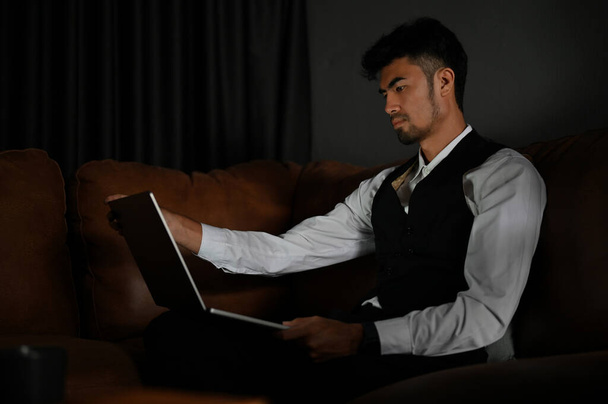 Розумний азіатський бізнесмен або професійний чоловічий менеджер фінансових інвестицій у формальному костюмі сидить на шкіряному дивані і використовує ноутбук
. - Фото, зображення
