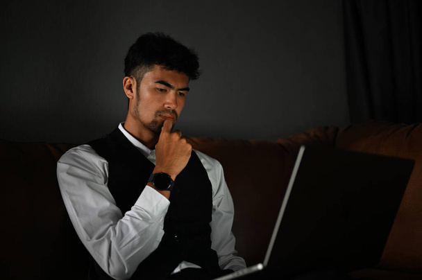 Pensativo adulto asiático hombre de negocios o gerente ejecutivo pensativo pensando en el plan de negocios, utilizando el ordenador portátil en su oficina. - Foto, imagen