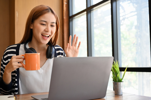 Aantrekkelijke jonge Aziatische vrouwelijke student of freelancer met een online ontmoeting op draagbare laptop computer, werken op afstand in de coffeeshop. - Foto, afbeelding