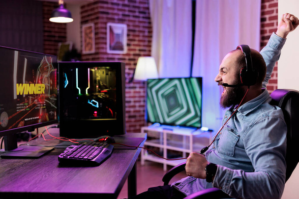 Νεαρό πρόσωπο γιορτάζει τα βιντεοπαιχνίδια κερδίσει στο τουρνουά, παίζοντας online δράση rpg gameplay. Ευτυχισμένος ενήλικας αισθάνεται ευχαριστημένος για τη νίκη πρωτάθλημα τυχερών παιχνιδιών, χρησιμοποιώντας υπολογιστή για να stream και να παίξει. - Φωτογραφία, εικόνα