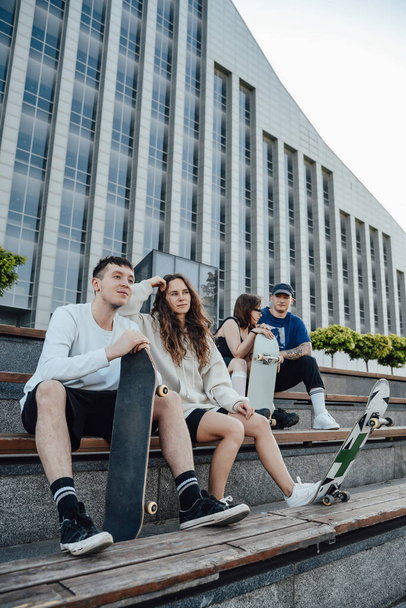Tiro de cuatro jóvenes amigos con patinetas al aire libre en la calle de la ciudad durante el día. - Foto, Imagen