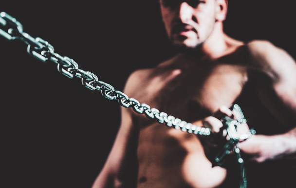 Muscular guy with chains on shoulders against a black background - Foto, Imagem