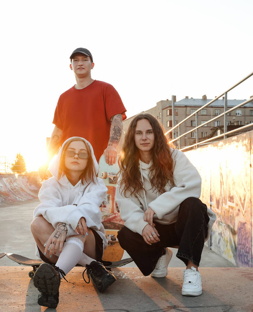 Opname van drie trendy vrienden in het urban skatepark samen naar de camera kijken. - Foto, afbeelding