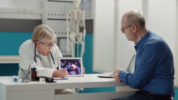 Female physician holding digital tablet with coronavirus animation, explaining pandemic disease to retired person at checkup visit. Virus illustration on device screen, covid 19 prevention. - Footage, Video