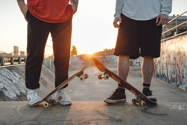 Retrato de dos chicos hipster tatuados con patinetas en skatepark al atardecer. - Foto, imagen