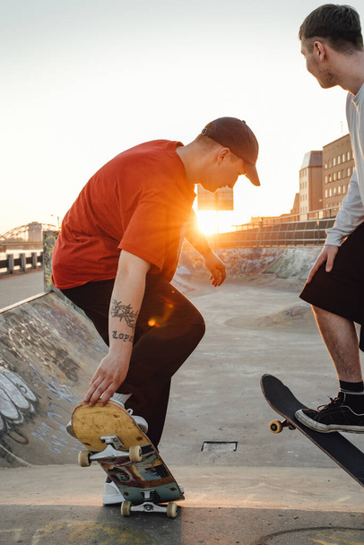 Shot of two tattooed hipster boys skateboarding at skate park at sunset. - Photo, Image