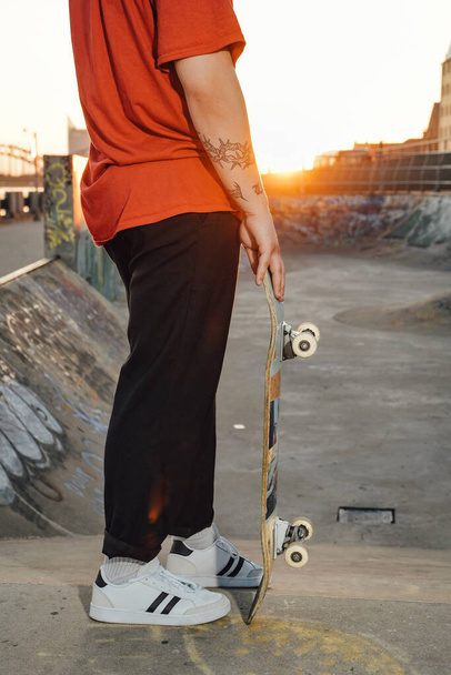 Portret van een jonge schaatser gekleed in casual kleding met skateboard op skatepark. - Foto, afbeelding