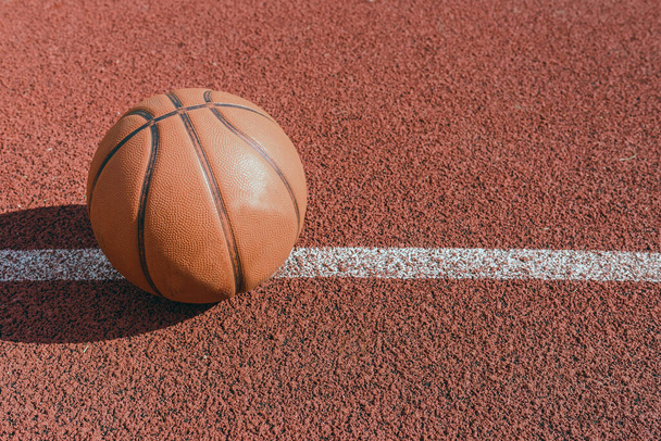 Oud oranje bal voor basketbal liggend op de rubberen sportveld.Sport rode grond buiten in de tuin.Bovenaanzicht, Kopieer ruimte. - Foto, afbeelding