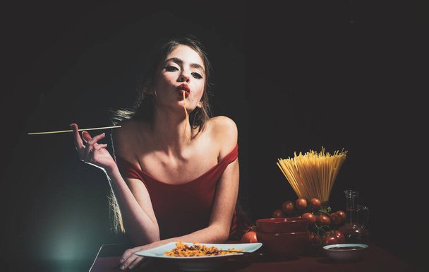 Young sexy woman eating tasty pasta on black - Zdjęcie, obraz