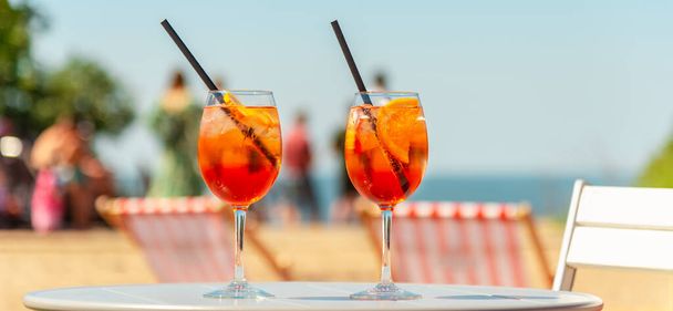 Banner, Werbung. Zwei Gläser Orangenspritz Aperol Drink Cocktail auf Tisch im Freien mit Blick auf Meer und Bäume verschwommenen Hintergrund. - Foto, Bild