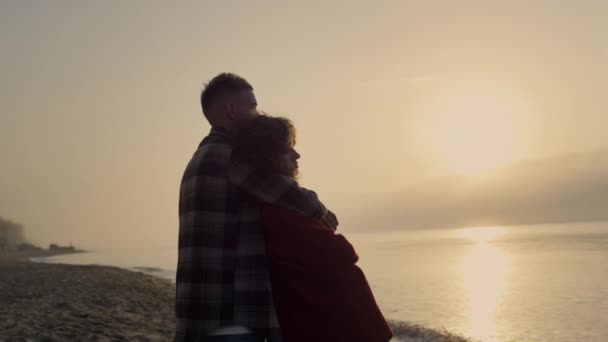 Romantická žena a muž stojící za úsvitu na pláži. Milující pár si spolu užívají výhled na moře. Zasněný přítel objímající přítelkyni. Sluneční paprsky dopadají na hladinu oceánu během západu slunce. Letní koncept  - Záběry, video