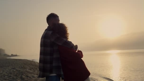 Romanttinen pari näyttää auringonlaskua rannalla takaisin näkymä. Kaunis nainen ottaa kuvia merestä auringonnousun aikaan. Ihana mies ja tyttö halailemassa yhdessä. Unelmoivat rakastavaiset viettävät kesälomaa meressä. Matkustuskäsite - Materiaali, video