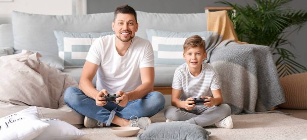 Ο πατέρας και ο γιος του παίζουν βιντεοπαιχνίδια στο σπίτι. - Φωτογραφία, εικόνα