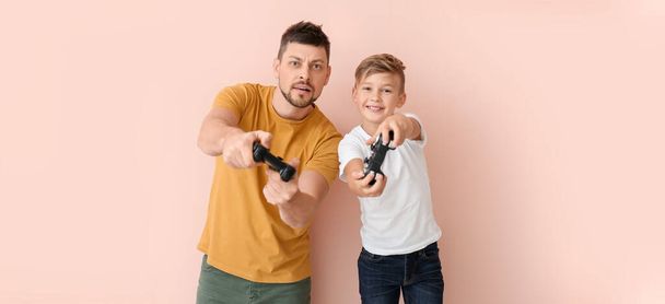 Father and his little son playing video games on color background - Foto, Imagen