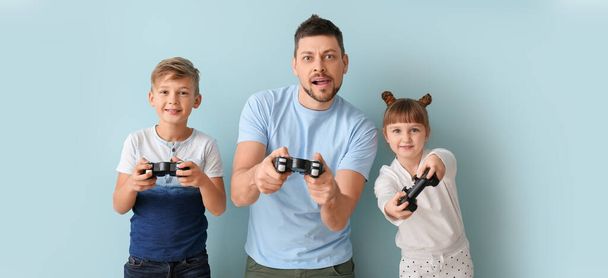 Vater und seine kleinen Kinder spielen Videospiele auf hellblauem Hintergrund - Foto, Bild