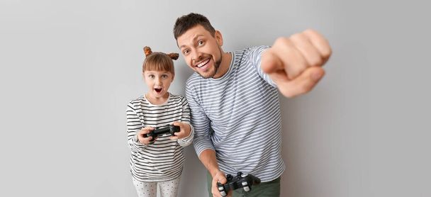 Pai e sua filhinha jogando videogames em fundo cinza
 - Foto, Imagem