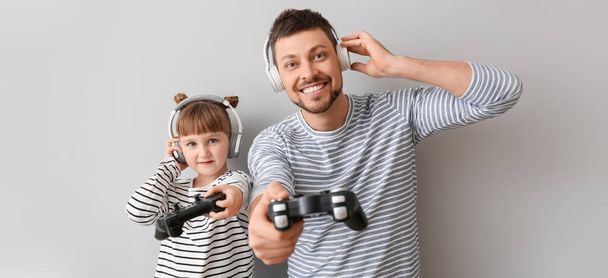 Father and his little daughter playing video games on grey background - Photo, Image
