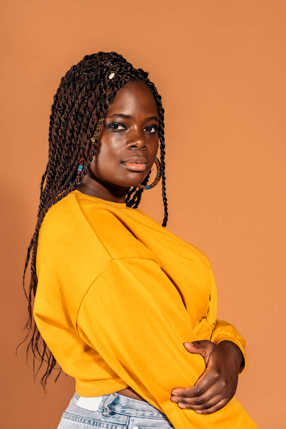 Stock photo of confident black woman with braids posing in studio shot against brown background. - Photo, image