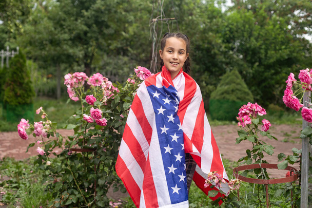 Patriotisches weibliches Kind mit amerikanischer Flagge in den Händen. Gegen bewölkten Himmel. Hochwertiges Foto - Foto, Bild