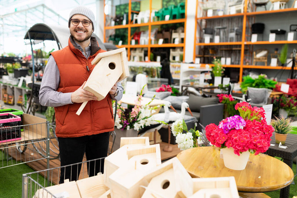 a satisfied customer in a garden and garden supply store holds a birdhouse in his hands. - Photo, Image