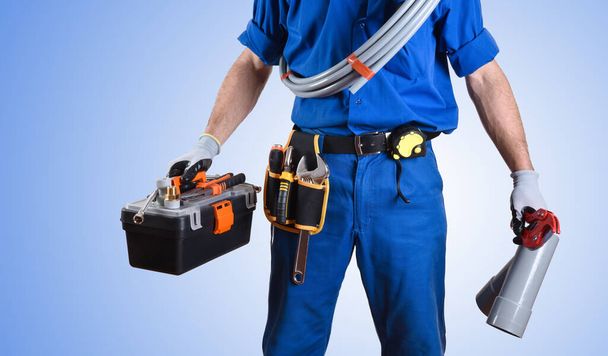 Detail of uniformed plumber with work tools in hands and blue gradient isolated background. Front view. Horizontal composition. - Foto, Bild