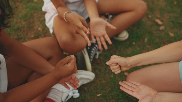 Close-up of the hands of three girls friends pre-teenage sitting on the grass in the park playing Rock-paper-scissors - Foto, immagini