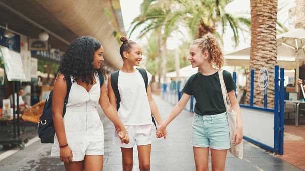 Three girls friends pre-teenage stand on the street smiling and emotionally talking holding hands. Three teenagers on the outdoors in urban citiscape background - Foto, immagini