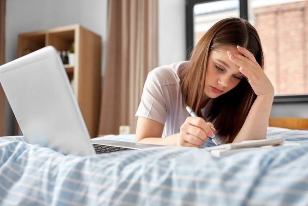 school, education and stress concept - tired teenage student girl with laptop computer and notebooks lying on bed at home - Φωτογραφία, εικόνα