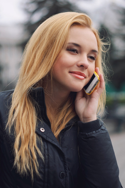 Encantadora chica rubia sonríe y habla por teléfono móvil
 - Foto, Imagen