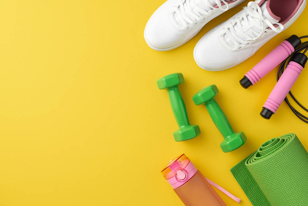 Αθλητική ιδέα. Top view φωτογραφία του ροζ skipping σχοινί μπουκάλι νερό αλτήρες πράσινο σπορ χαλάκι και λευκά sneakers σε απομονωμένο κίτρινο φόντο με κενό χώρο - Φωτογραφία, εικόνα