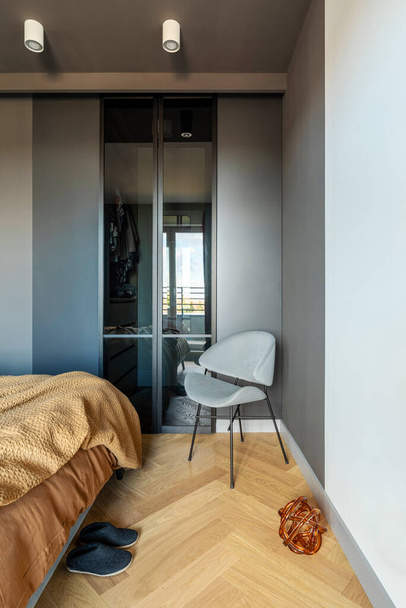 Stylish composition of modern bedroom interior. Wardrobe , grey chair and elegant personal accessories. Grey wall. Brown sheeets. Minimalistic masculine concept. Template. - Foto, immagini
