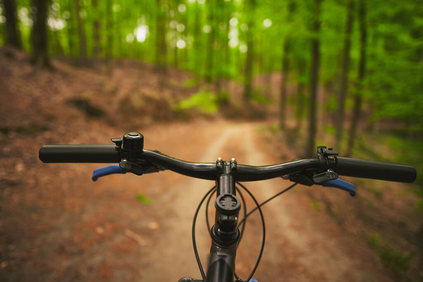 Vista en primera persona de la manipulación de la bicicleta en el camino forestal vacío hacia la luz del sol. Ciclismo al aire libre durante la soleada noche de verano - Foto, Imagen