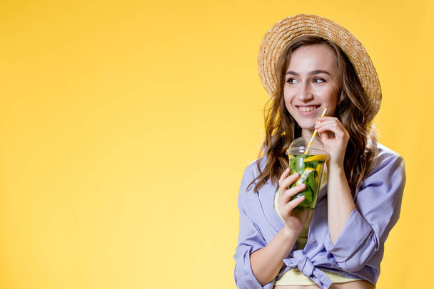 Woman in summer outfit wearing white trendy sunglasses and enjoying while drinking a Mojito cocktail. Posing on the yellow background. - Foto, Bild