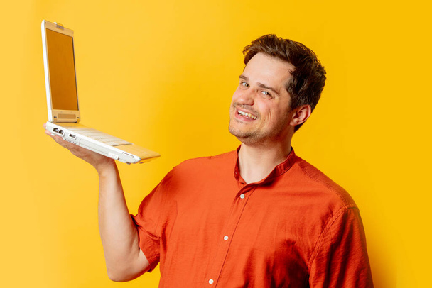 Stylish man in orange shirt with laptop computer on yellow background - Photo, Image