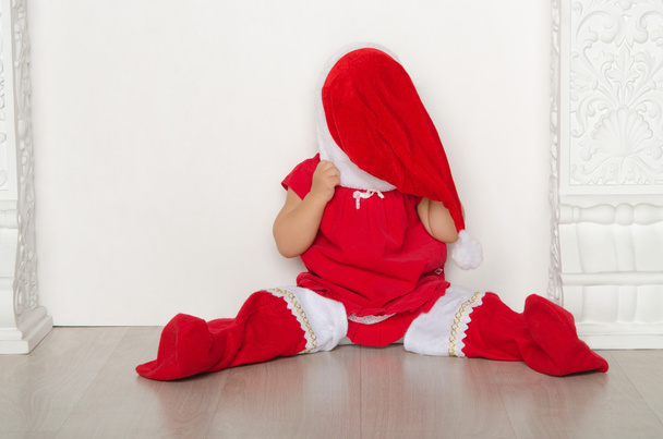Girl in costume of Santa closes face sitting on floor - Photo, image