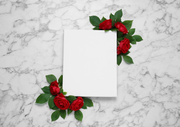 Blank canvas and beautiful red roses on white marble table, flat lay. Space for design - Zdjęcie, obraz