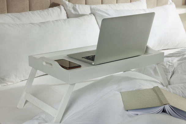 White tray with modern laptop and smartphone on bed indoors - Foto, Bild