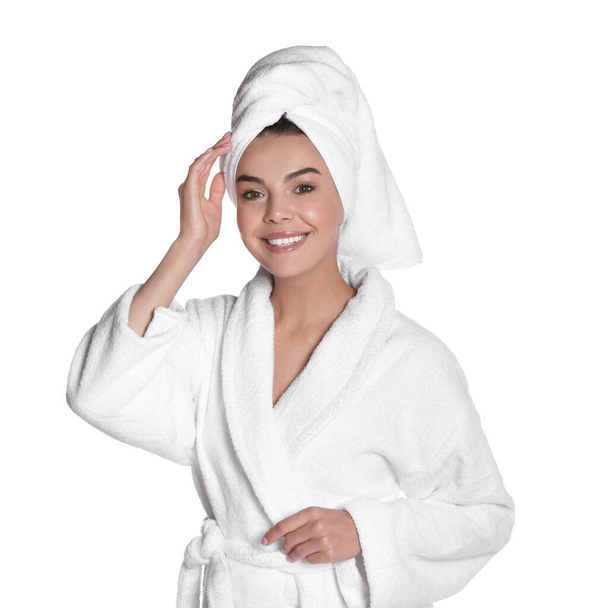 Beautiful young woman wearing bathrobe and towel on head against white background - Foto, Imagem