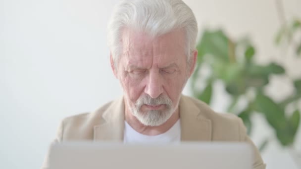 Κοντινό πλάνο του ηλικιωμένου που κοιτάζει την κάμερα ενώ χρησιμοποιεί το lap-top στο γραφείο - Πλάνα, βίντεο