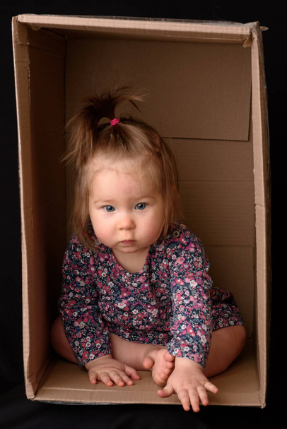 Feliz niña sentada en una caja de cartón y divirtiéndose - Foto, Imagen