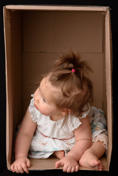 Happy little girl sitting in a cardboard box and having fun - Фото, изображение