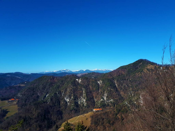 Vista panorámica de la montaña Tosc en las colinas de Polhov Gradec, Eslovenia y picos nevados de los Alpes Julianos en el fondo - Foto, Imagen