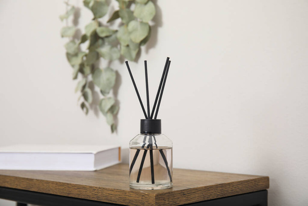 Reed diffuser and book on wooden table near white wall - Foto, Imagem