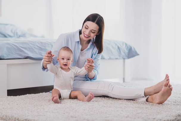 Portrait of attractive cheerful woman playing with toddler having fun sitting on floor carpet staying home indoors. - Foto, immagini