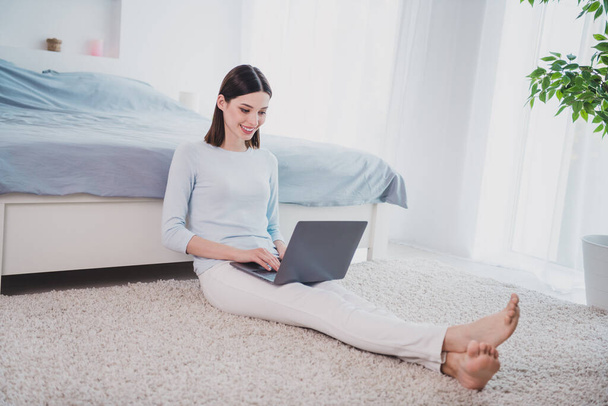 Portrait of attractive cheery focused woman sitting on soft carpet using laptop writing email eshop staying home indoors. - Foto, Imagem