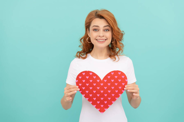 smiling redhead woman hold red heart on blue background. - 写真・画像