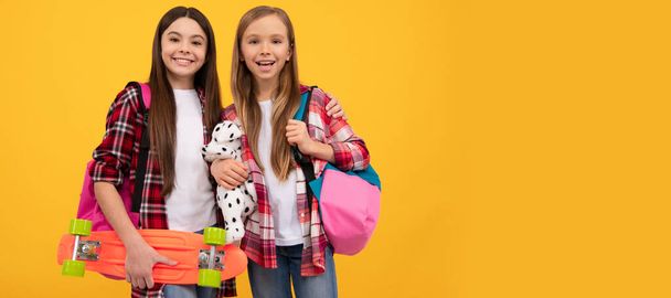 School girls friends. happy kids in casual checkered shirt carry backpack toy and penny board, casual lifestyle. Portrait of schoolgirl student, studio banner header. School child face - 写真・画像