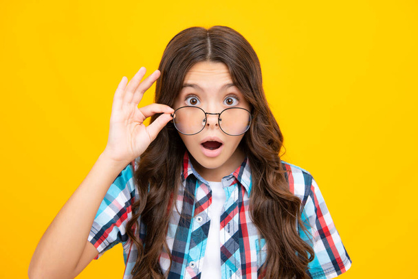 Shocked surprised teenager girl. Teenager child wearing glasses on yellow studio background. Cute girl in eyeglasses - Photo, Image