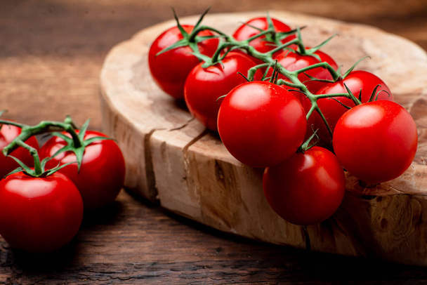 Branch of fresh cherry tomatoes on a brown wooden background. - Foto, afbeelding