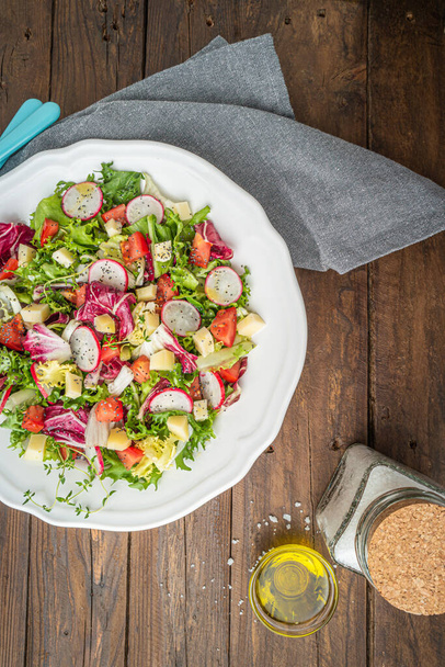 Frischer Salat mit gemischtem Rettichkäse und Tomaten auf einem Teller auf Holzboden. Italienische mediterrane oder griechische Küche. Vegetarisches veganes Essen. - Foto, Bild